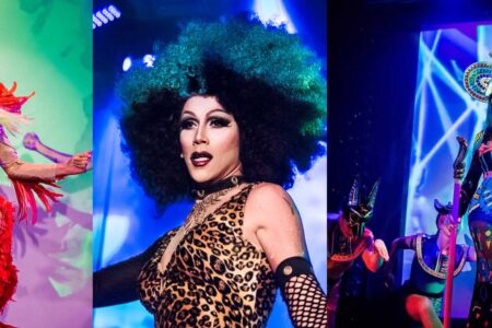 Three drag performers on stage in vibrant costumes. The first wears a gold and red outfit with feather accents, the second sports a leopard print dress with a large green and black wig, and the third dons an elaborate headdress and colorful ensemble.