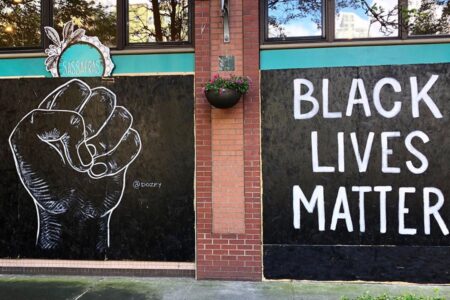 A mural on a brick wall features a raised fist painted in white on a black background, with the words 