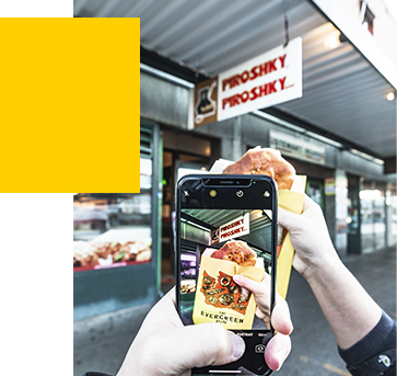 A person using their camera to take a photo of a piroshky in front of the Piroshky Piroshky storefront