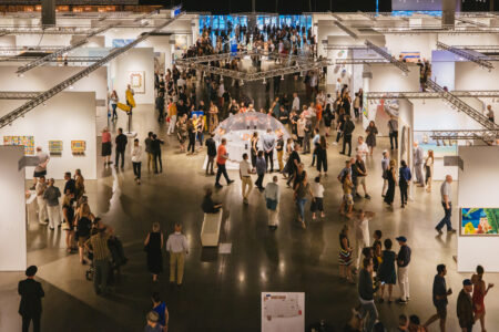 A crowd of people walking around a large space with white gallery walls.