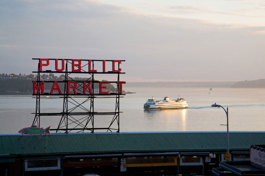 A ferry sails across the blue waters of Elliott Bay behind the red Public Market sign.