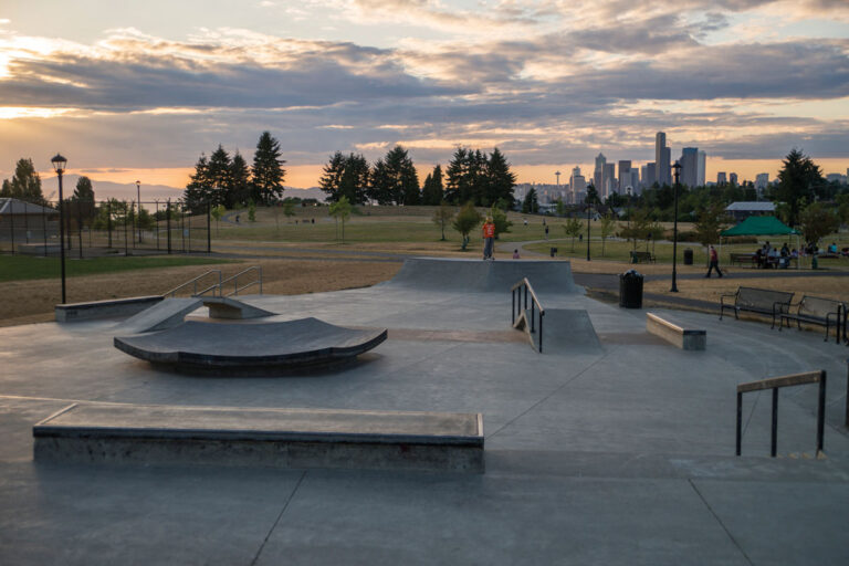 A kid in a red shirt rides their scooter in a skate park.