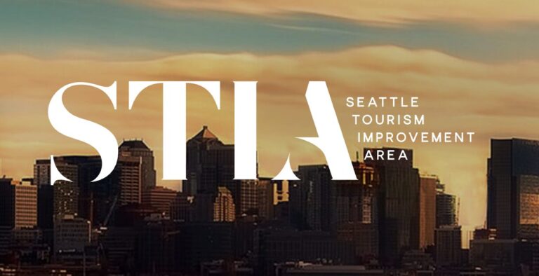 The image shows a city skyline under a dramatic, orange sky with large white text reading "STIA" and smaller text beside it: "Seattle Tourism Improvement Area.