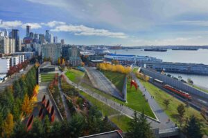 Aerial view of Seattle’s Olympic Sculpture Park with green lawns, walking paths, and sculptures, bordered by city buildings on the left.