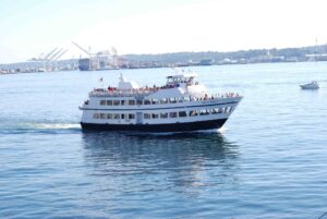 A white and blue passenger ferry filled with people sails on a calm body of water. 