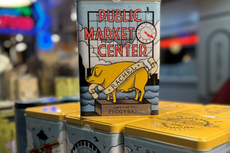A rectangular tin piggy bank decorated with the Pike Place Market sign and a yellow pig labeled 