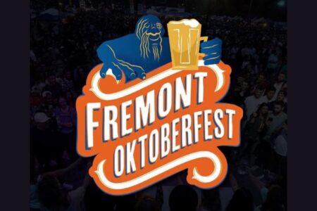 A colorful Fremont Oktoberfest logo featuring a blue creature holding two beers overlays a background of a large, festive crowd gathered at an outdoor event.