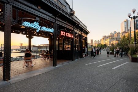 People walk along a waterfront promenade near a building with neon signs for 