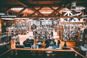 A spacious, well-lit Seattle 2026 bookstore with wooden floors and beams, filled with bookshelves and several people browsing or talking. Large windows let in natural light, creating a warm, inviting atmosphere.