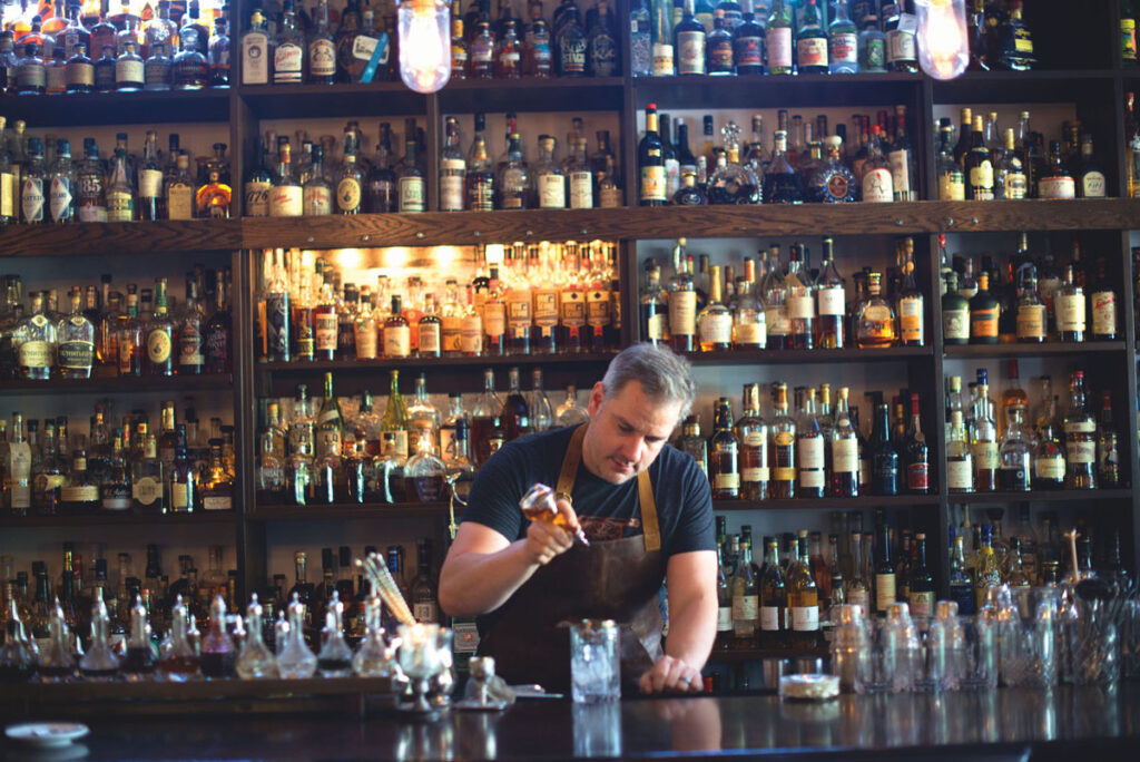 A man in an apron pouring liquid into a glass.