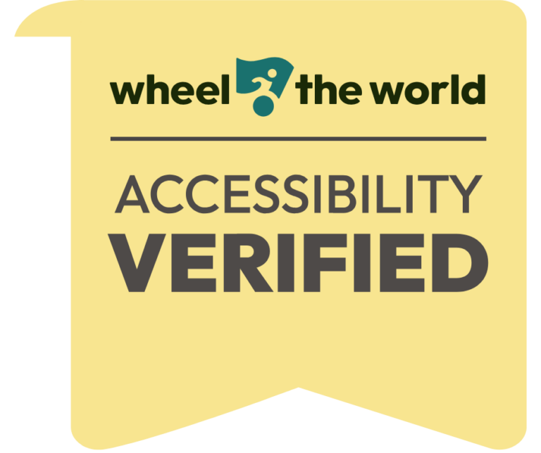 A yellow badge with the text “wheel the world” above a dividing line, and “ACCESSIBILITY VERIFIED” in bold letters below, indicating certification for accessibility.
