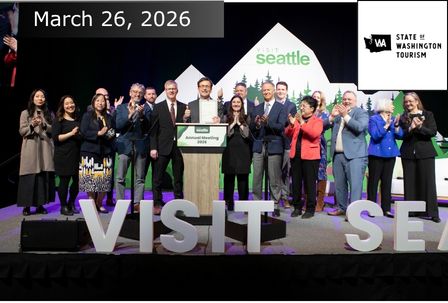A group of people stand on stage at a Visit Seattle event, clapping and smiling behind a podium. Large letters reading "VISIT SEA" are in front. The date "March 26, 2026," and a Washington Tourism logo are displayed.