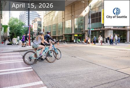 Two cyclists wait at a crosswalk on a busy city street in Seattle. Pedestrians walk on the sidewalk; modern buildings line the background. Text reads "April 15, 2026" and "City of Seattle" with the city logo.