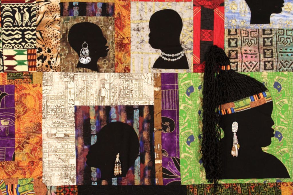 A vibrant quilt features black silhouette profiles adorned with jewelry and headpieces, set against colorful, patterned fabric squares inspired by African and Egyptian art. One profile includes textured black hair.
